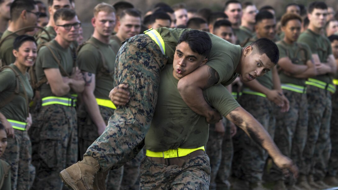 One Marine carries another over his shoulders as fellow Marines observe.