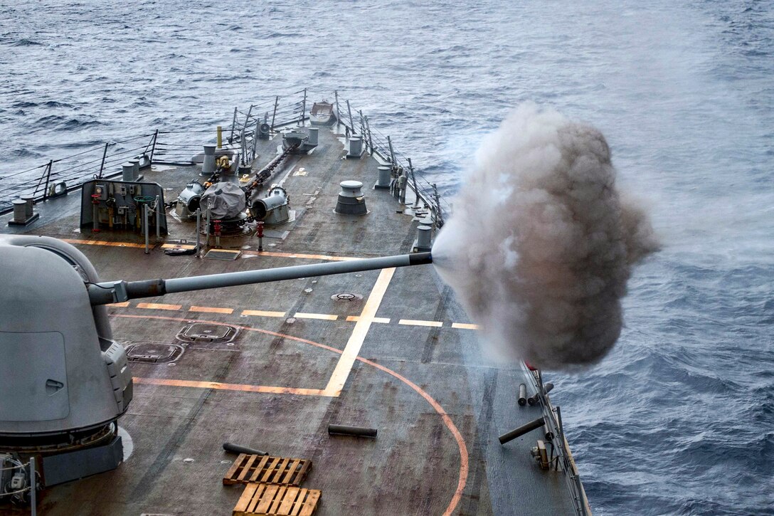 A gun aboard a ship at sea fires a projectile.