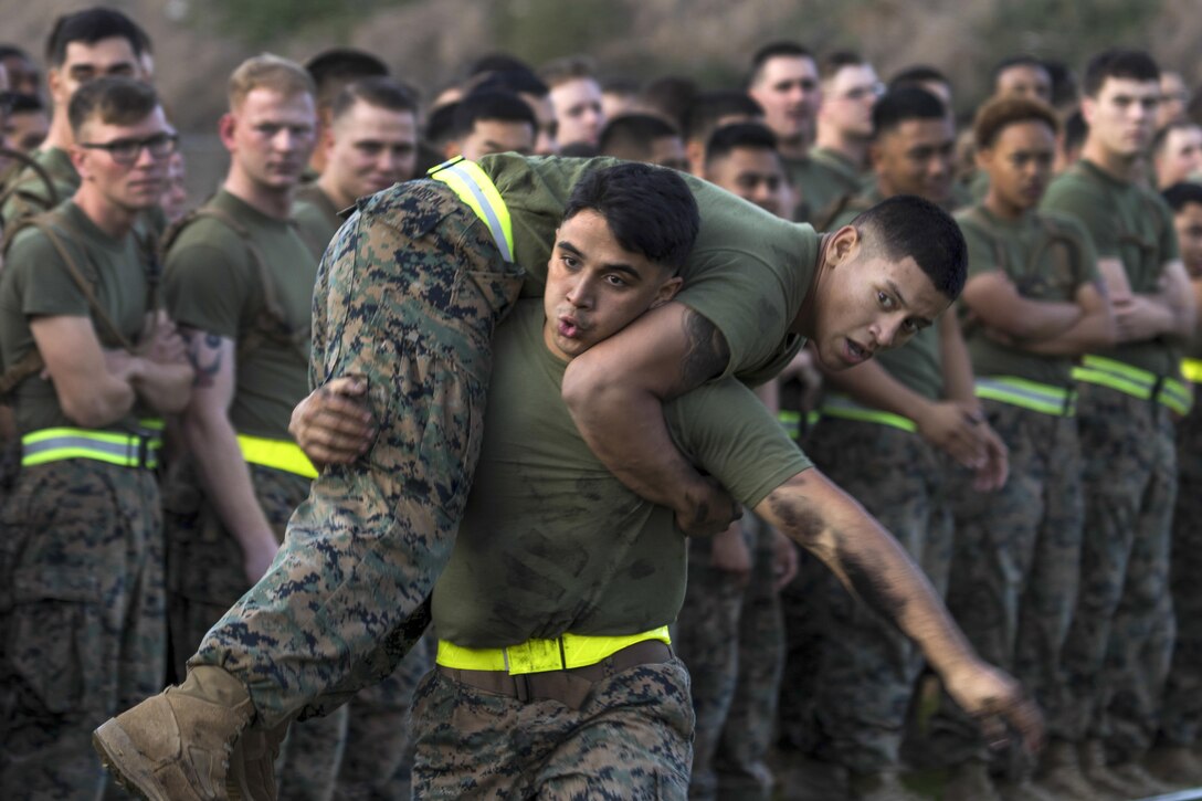 One Marine carries another over his shoulders as fellow Marines observe.