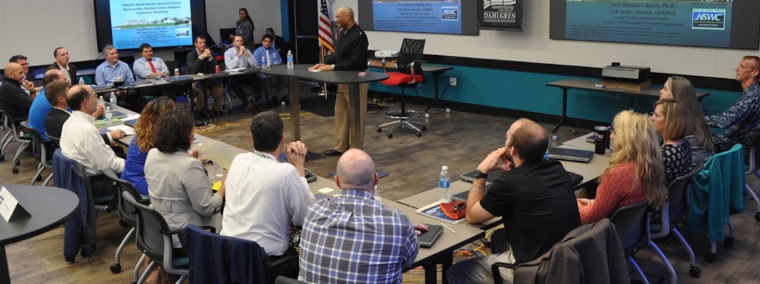 IMAGE: DAHLGREN, Va. - Rear Adm. Jesse Wilson, Naval Surface Force Atlantic commander, emphasizes the importance of innovating to the strategic environment as he spoke to a group of civilian technologists and military officers at the first in a series of Surface Warfare Innovation Workshops held at the Navy's newest Innovation Lab. Naval Surface Warfare Center Dahlgren Division (NSWCDD) and the Navy War College co-sponsored the event that encouraged NSWCDD scientists and engineers to throw away the rule book as they brainstormed to solve future warfighting scenarios. "The workshop enabled Navy leadership to share current and future Fleet concerns with our new and mid-career personnel to develop united, focused, and creative solutions," said NSWCDD I-Lab Director of Innovation Nelson Mills.