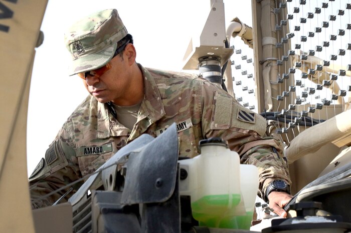 A person looks at the engine of a military vehicle.