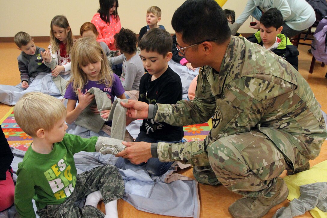 A soldier holds a bandage while teaching children first aid techniques.
