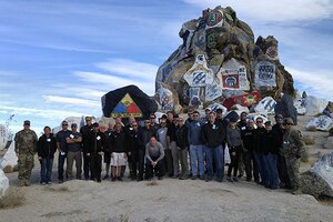 Business leaders pose in front of a large rock at Fort Irwin, California.