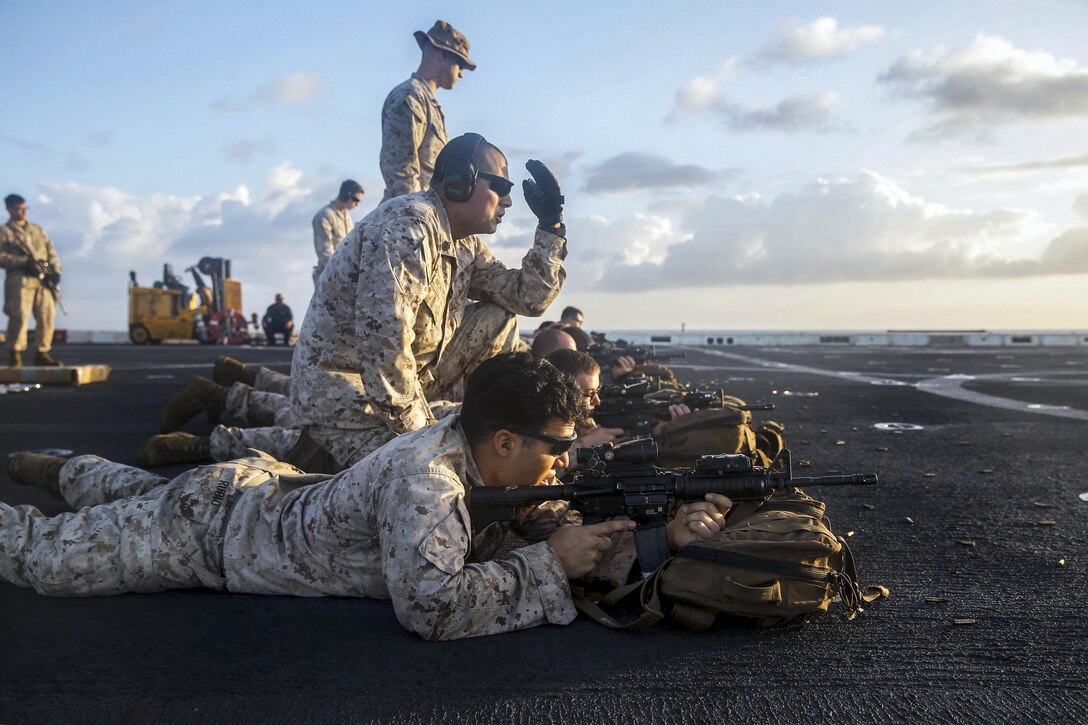 Marines participate in a live-fire exercise on a ship's deck.