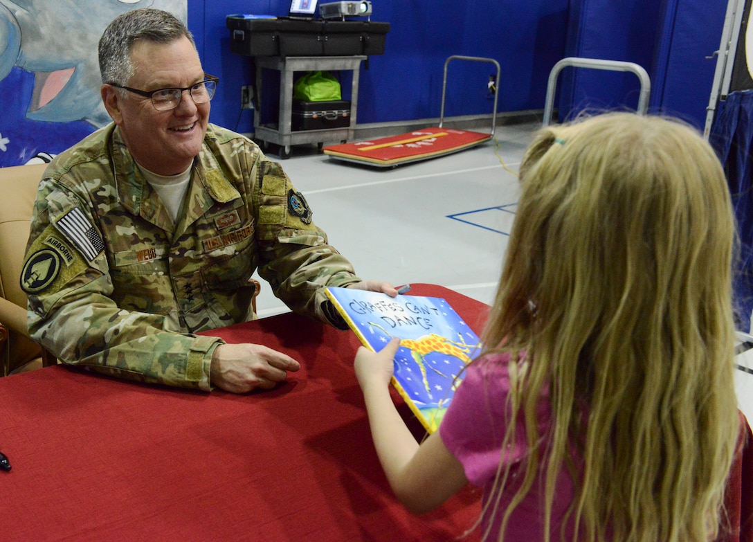 Lt. Gen. Brad Webb, commander of Air Force Special Operations Command, hands a book to one child.