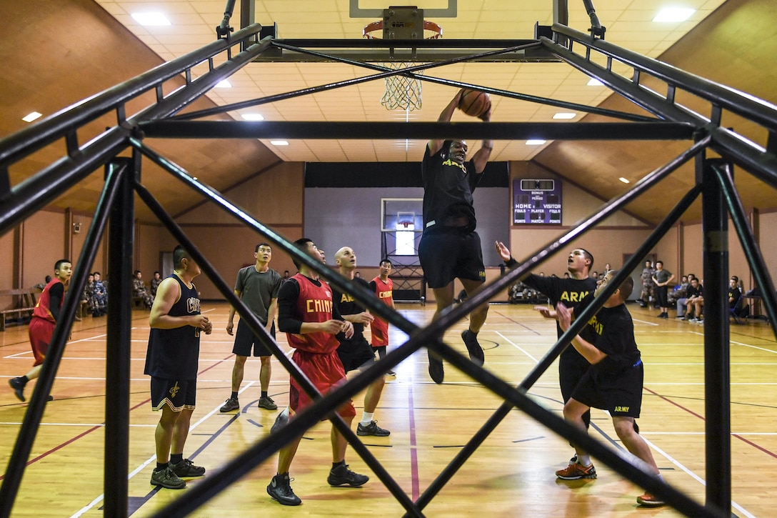 A service member jumps to take a shot during a basketball game, as others on the court watch.