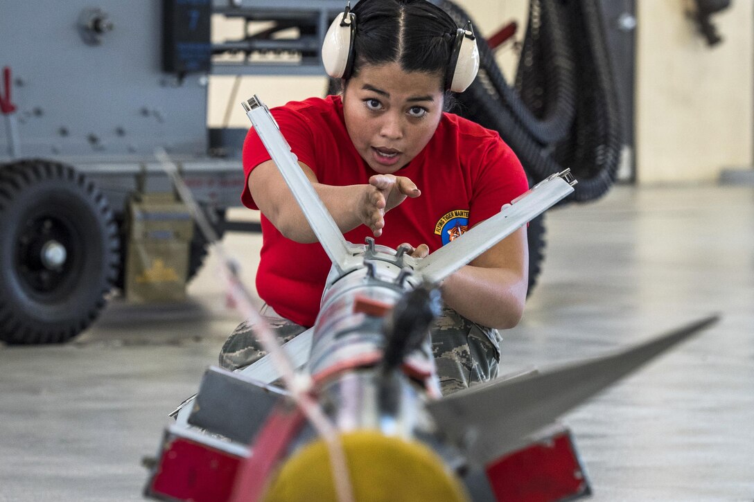 An airman speaks and gestures in a forward motion while inspecting a missile.