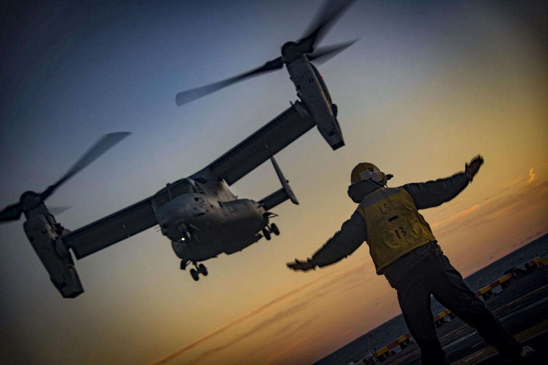 A sailor assists in the landing of an Osprey on a ship.