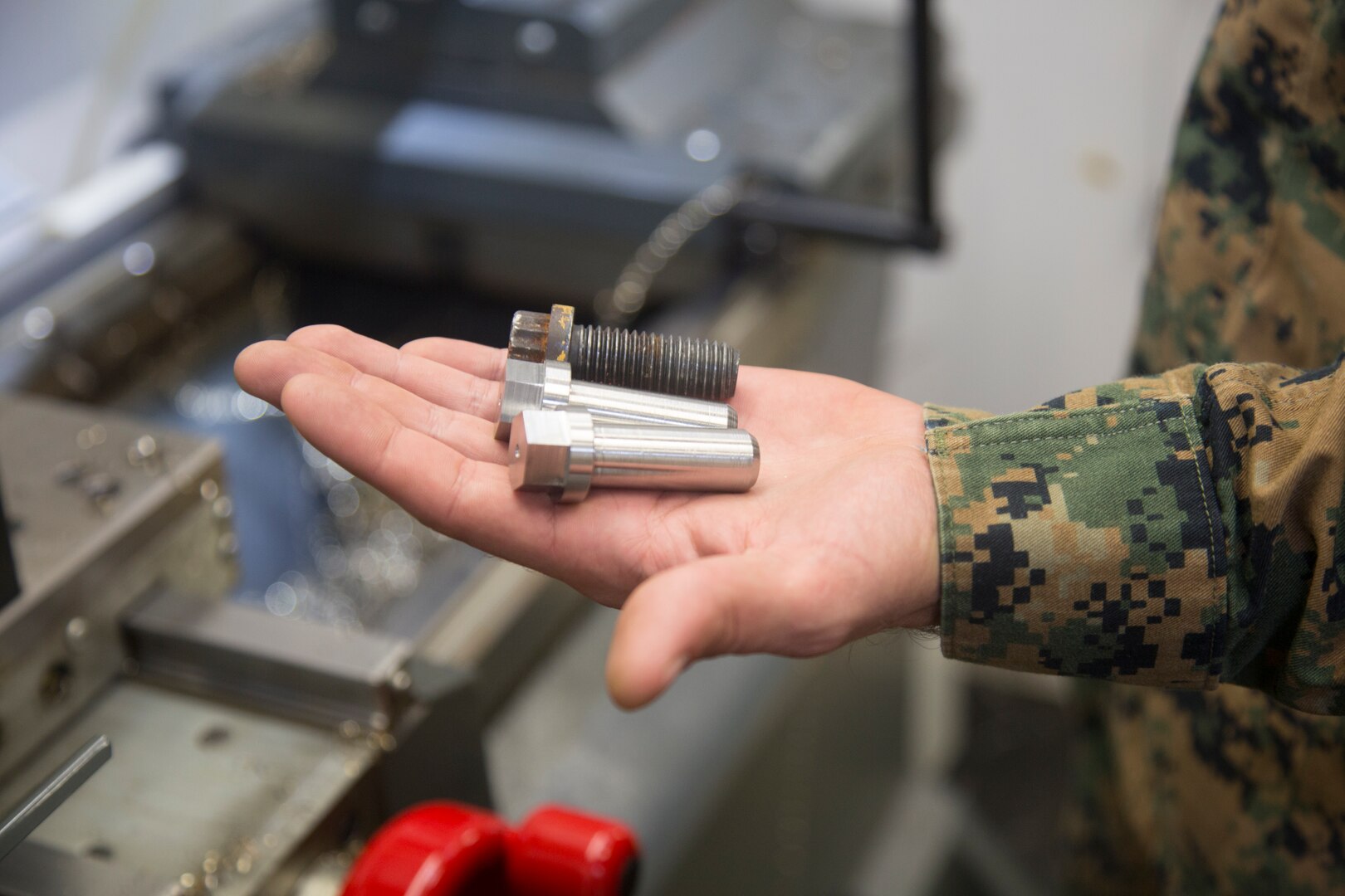 Gunnery Sgt. Justin A. Horn, the General Support Maintenance Company metal shop chief, holds untapped replacements for the removed, old rusty bolts, which will be fabricated to match the originals, Nov. 21, 2017, at Camp Kinser Okinawa, Japan. Marines at the GSM, 3rd Maintenance Battalion, 3rd Marine Logistics Group, make replacement hardware by using the TM1 CNC Mill machine, a mobile unit which allows the GSM Marines to accomplish their mission both at their duty stations and on exercise or deployment.