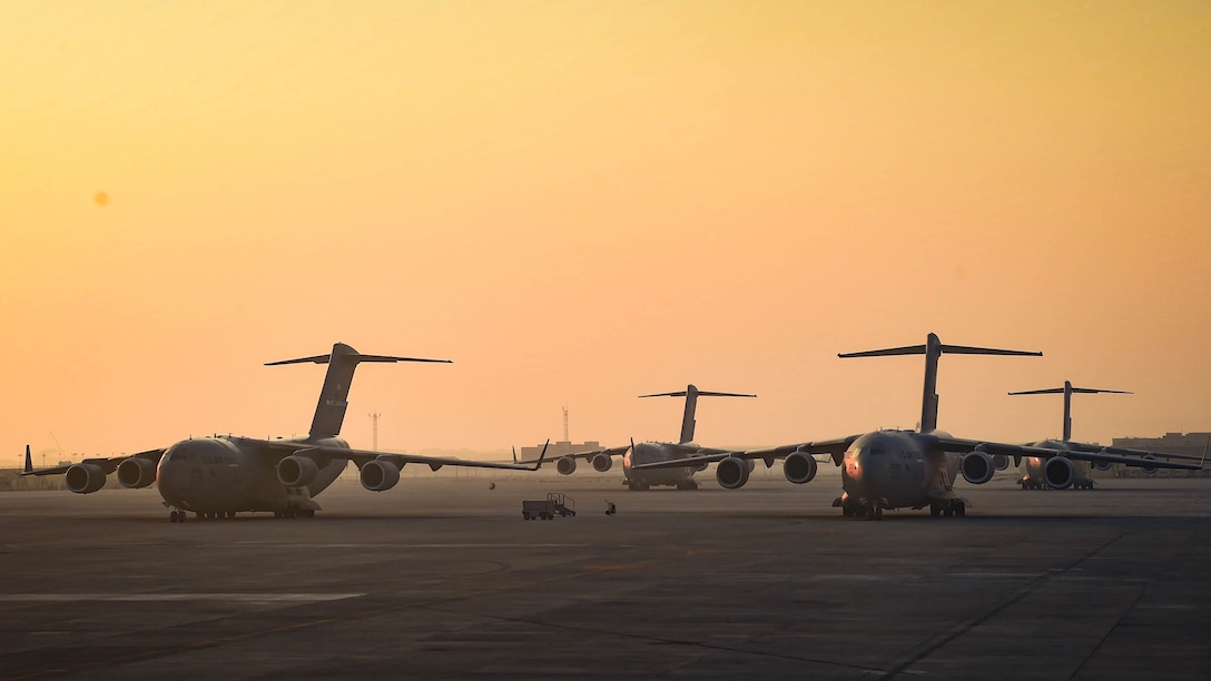 Military planes sit on a flight line with an orange sky in the background.