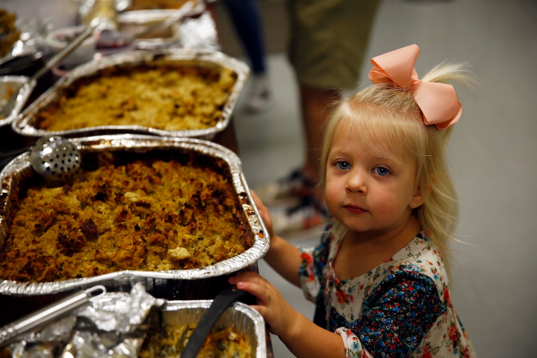 A little girl looks at  trays of food.