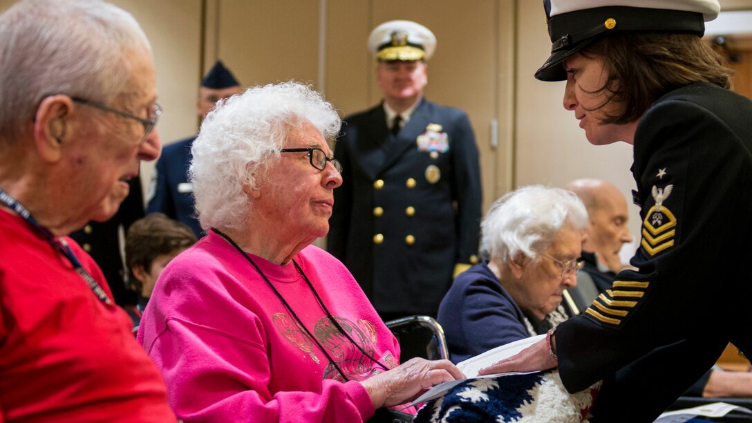 A sailor presents a retired service member with a blanket to publicly thank her.