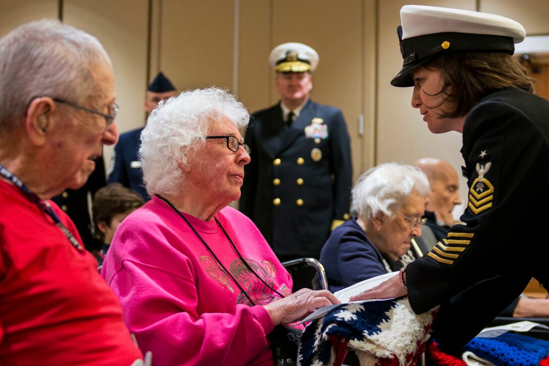A sailor presents a retired service member with a blanket to publicly thank her.
