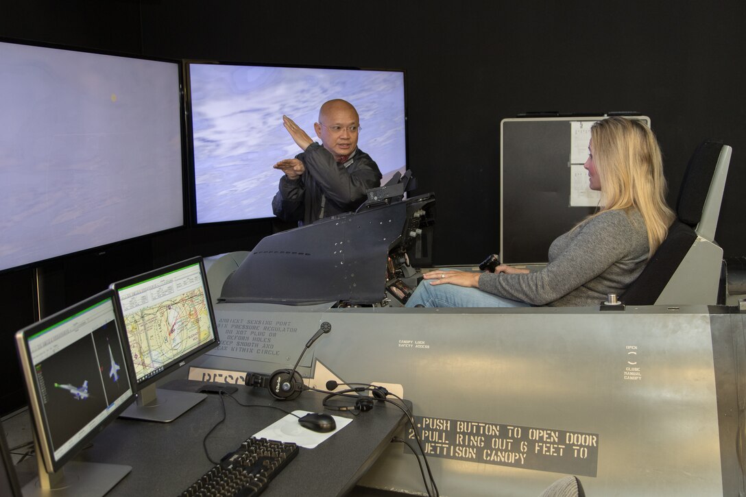 Aaron Fong, 412th Electronic Warfare Group, briefs Michelle West on her "mission" in the flight simulator during an Honorary Commanders' event at the Integrated Facility for Flight Avionics Systems Testing. (U.S. Air Force photo by Don Allen)