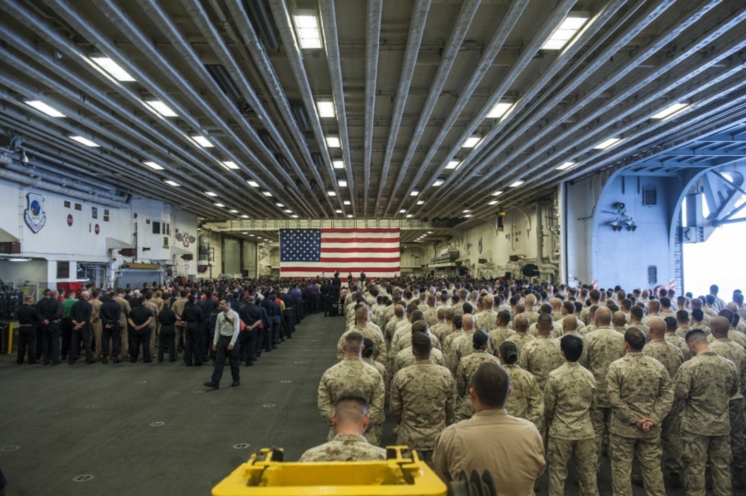 Secretary of the Navy Richard V. Spencer speaks to Sailors and Marines during all hands call in the hangar bay of the amphibious assault ship USS America during his visit on Thanksgiving Day.