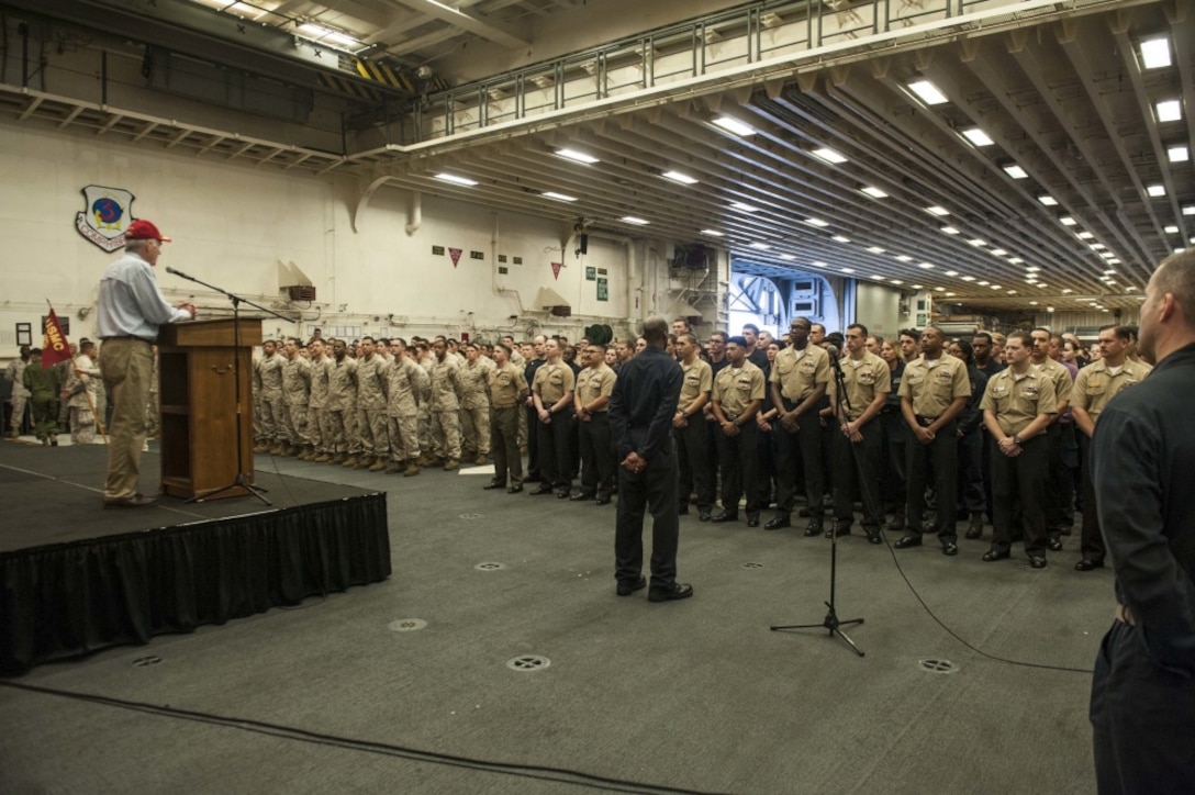 Secretary of the Navy Richard V. Spencer speaks to Sailors and Marines during all hands call in the hangar bay of the amphibious assault ship USS America during his visit on Thanksgiving Day.