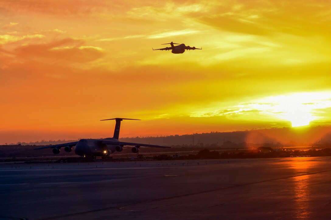 Military aircraft land and take off with a bright orange sky as a background.