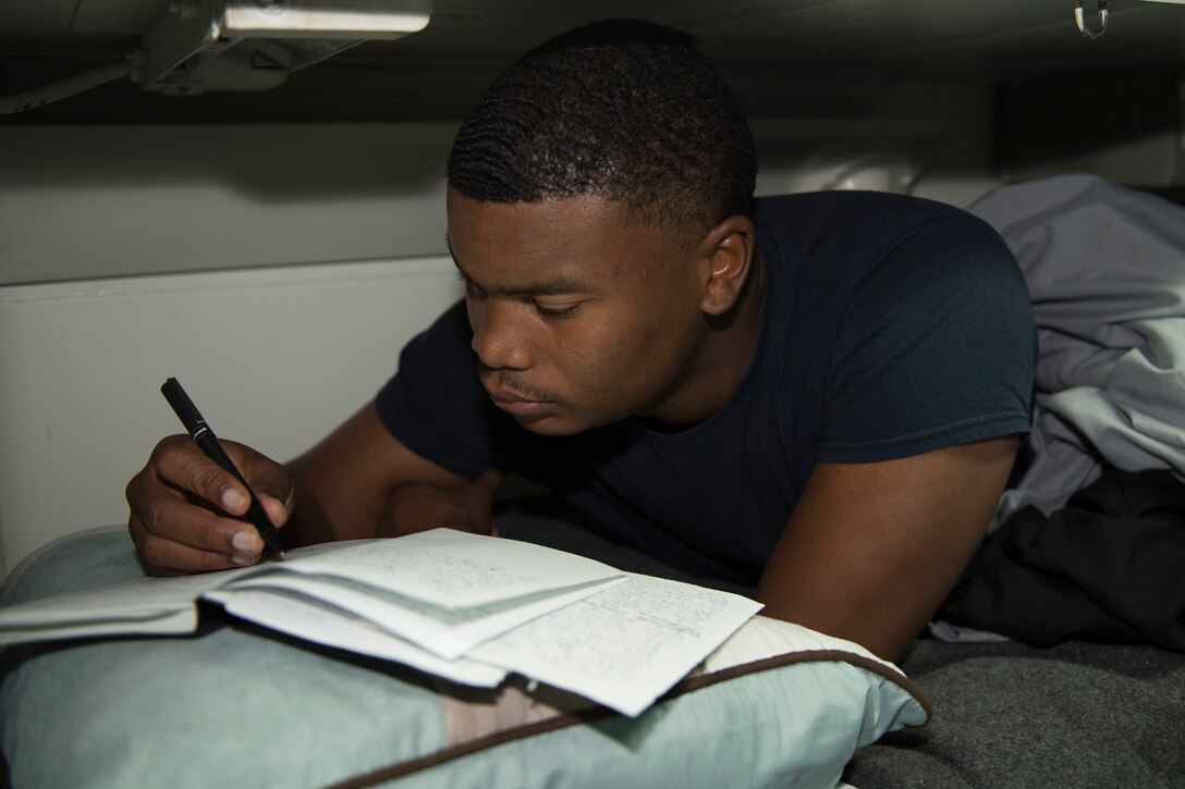 A sailor writes in a book while lying in bed.