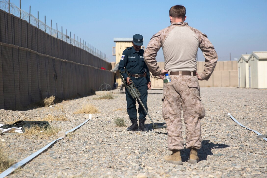 A U.S. Marine, foreground, observes and provides feedback as an Afghan national policeman clears a lane during lane training.