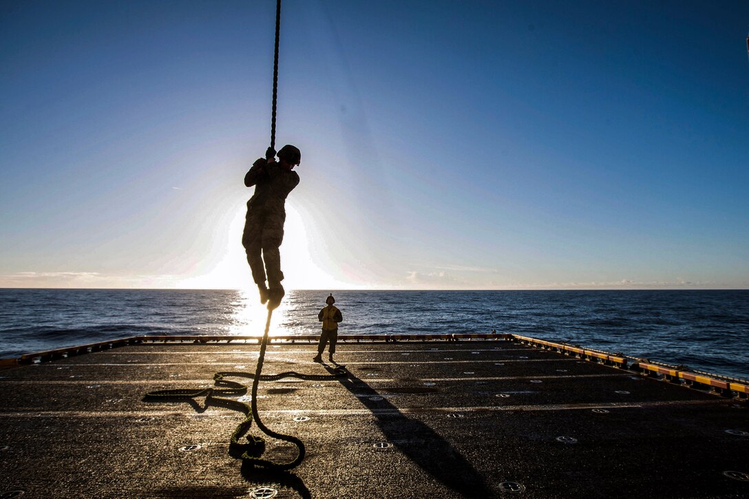 A Marine descends from a rope onto the deck of a ship.