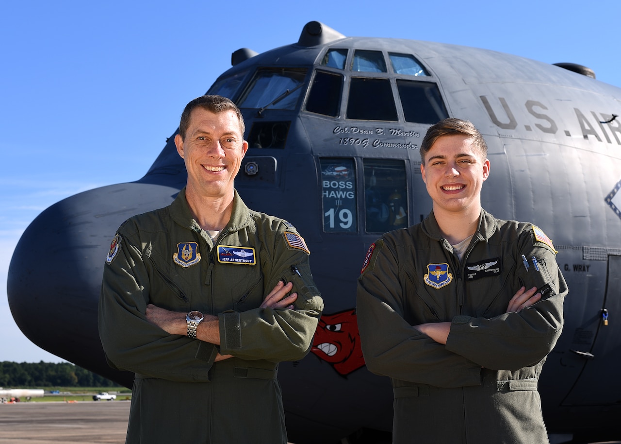 A father and son pose for a photo in front of a C-130 on a flightline.