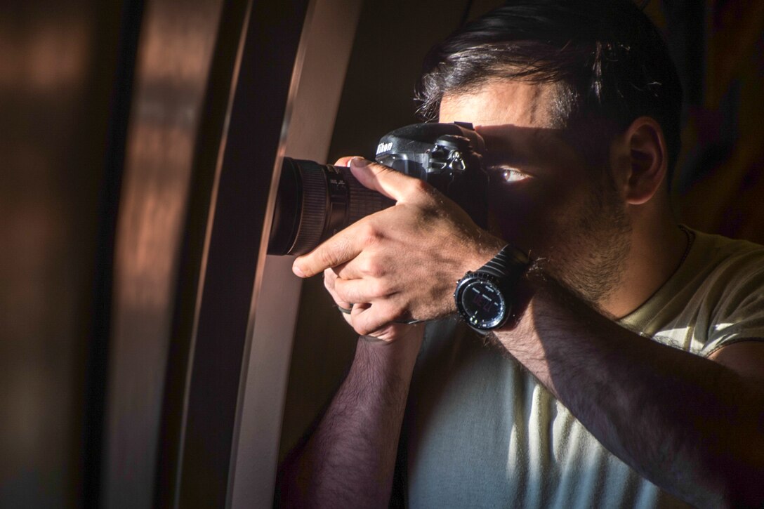 An airman photographs out the window of an aircraft.