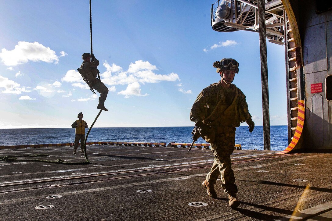 A Marine walks away as a team member participates in fast-rope training.
