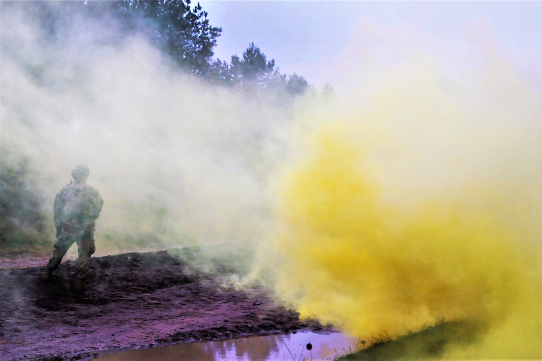 A soldier observes and evaluates his team members as they advance to their follow-on objective under the cover of smoke