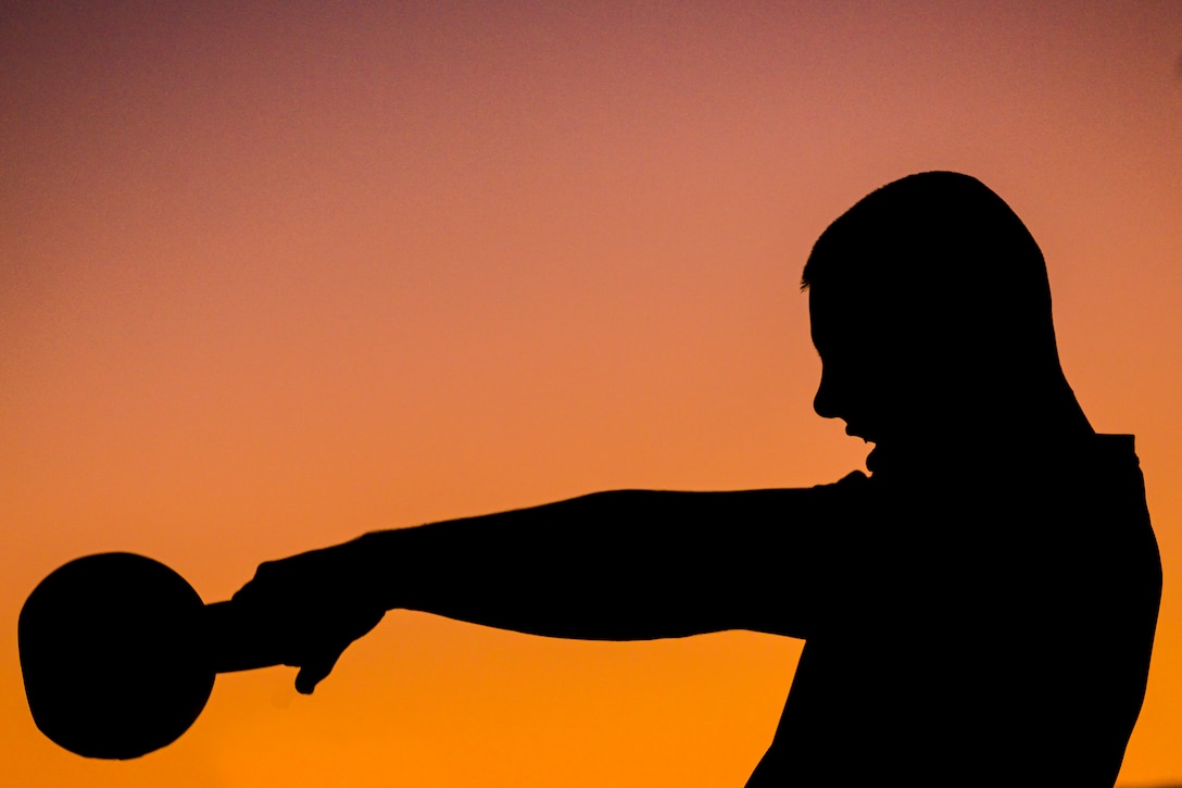 A silhouette of a person with workout equipment is against a colorful sky.