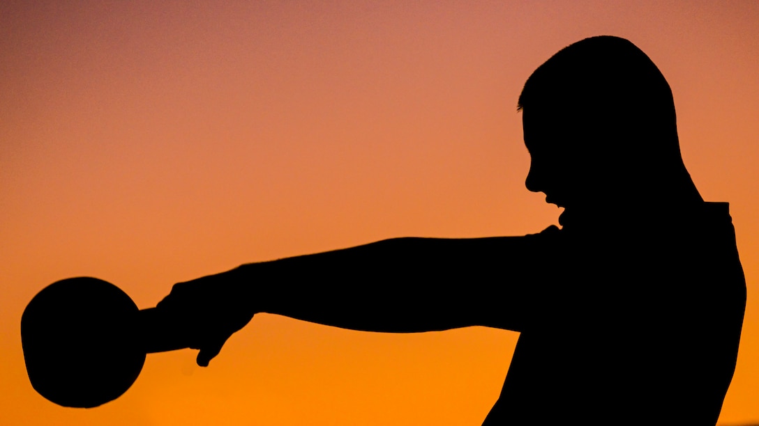 A silhouette of a person with workout equipment is against a colorful sky.