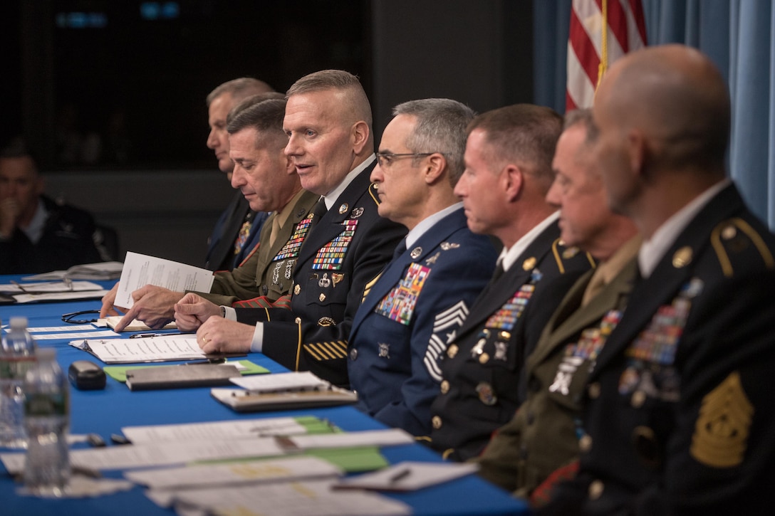 Military leaders sit at a long table and hold a news conference.