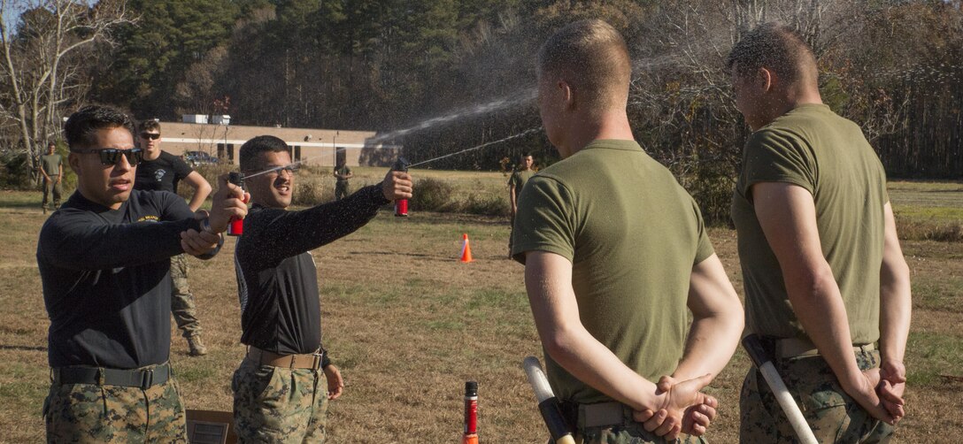 Staff Sgt. Omar Guzman, staff non-commissioned officer in charge, left, and Sgt. Brandon Bedard, instructor, Basic Security Guard Course, Training Co., U.S. Marine Corps Security Forces Regiment, spray oleoresin capsicum in the faces of students during the Level 1 OC Contamination Course at Naval Support Activity Northwest Annex, Chesapeake, Va., Nov. 28. Instructors were required to have OC training before being certified to use it on the students. (Official U.S. Marine Corps photo by Chris Jones/Released)