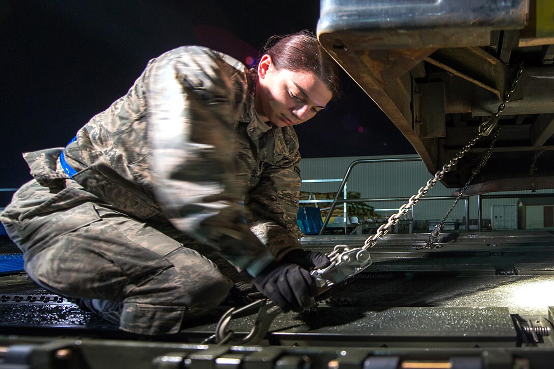 An airman uses chains to secure a bus.