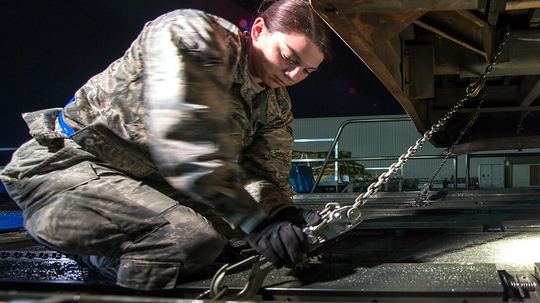 An airman uses chains to secure a bus.