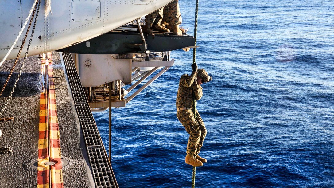 A Marine descends from an MV-22B Osprey during fast-rope training.