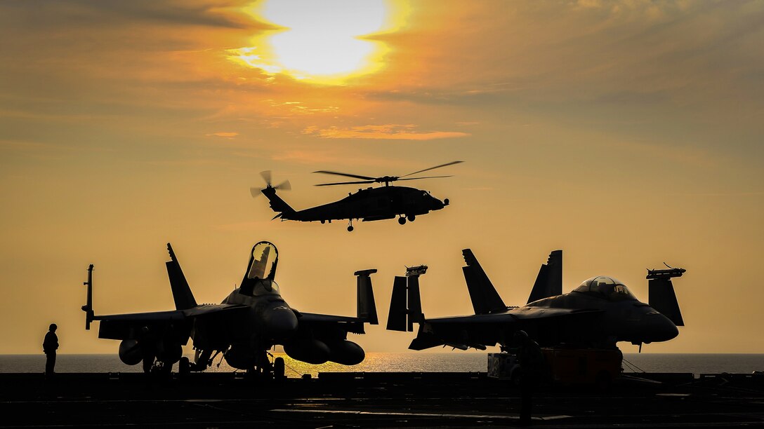 A helicopter lands in the background with two aircraft in the foreground.