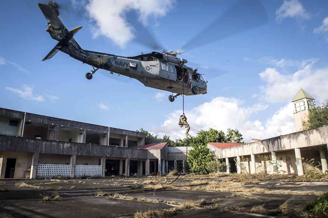 A soldiers uses a rope to slide from a helicopter.