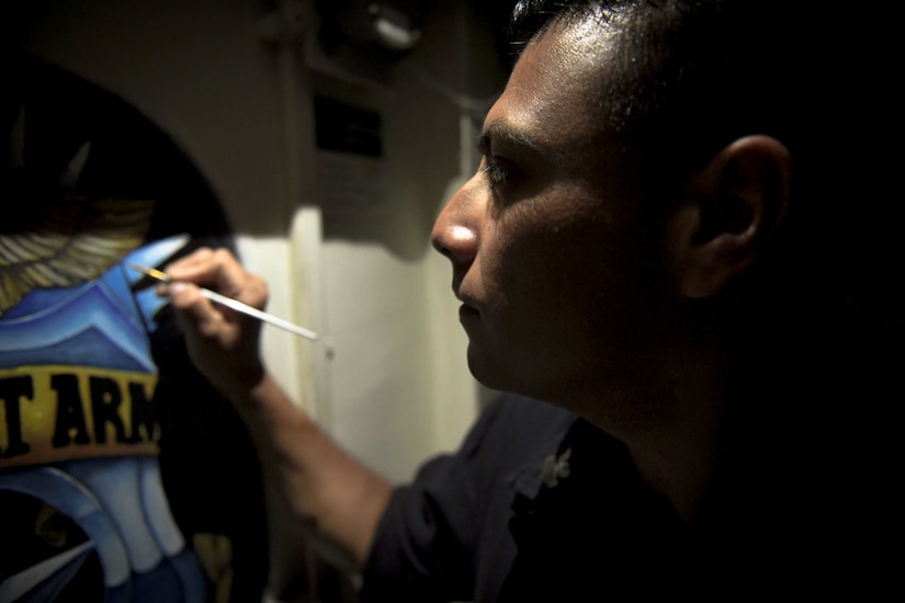 Navy Petty Officer 1st Class Juan Morales paints a mural on a door aboard the guided missile destroyer USS Kidd, Nov. 16, 2017. Navy photo by Petty Officer 2nd Class Jacob M. Milham