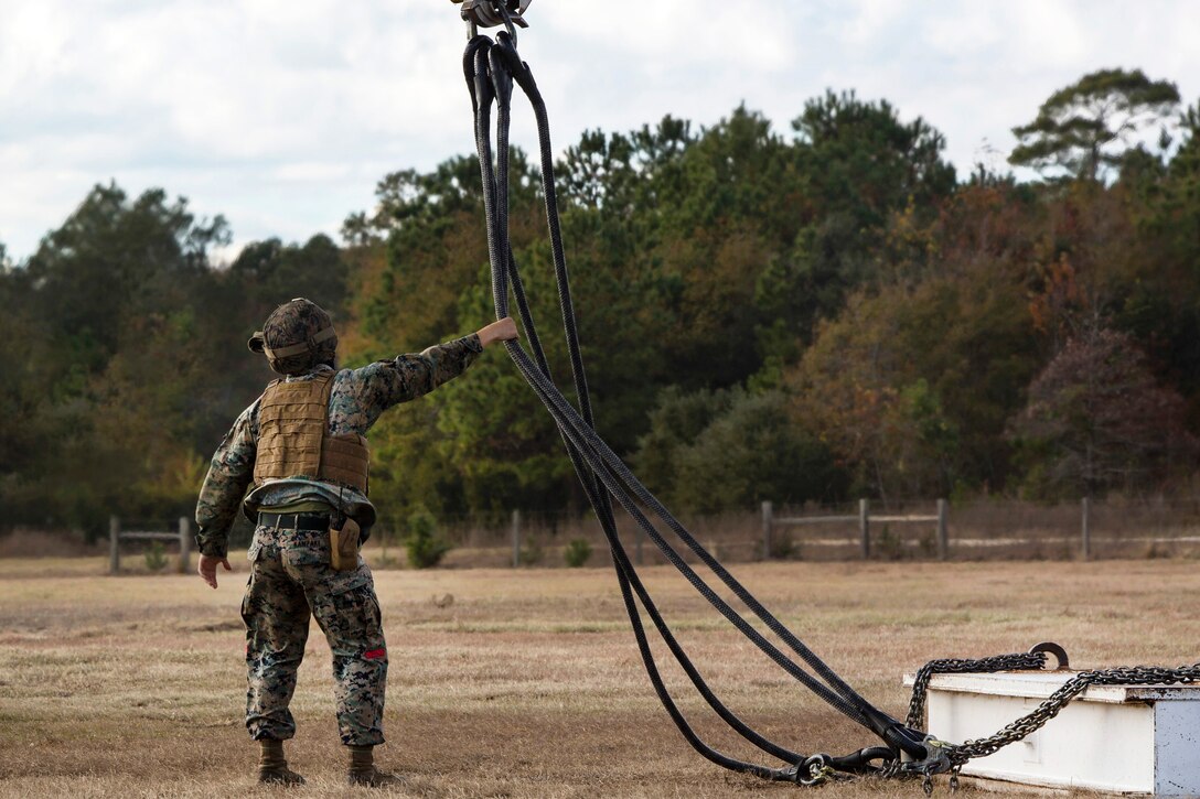 Marine Corps Cpl. James Kanzaki guides cables while a CH-53E Super Stallion helicopter lifts practice materials during hoist training.