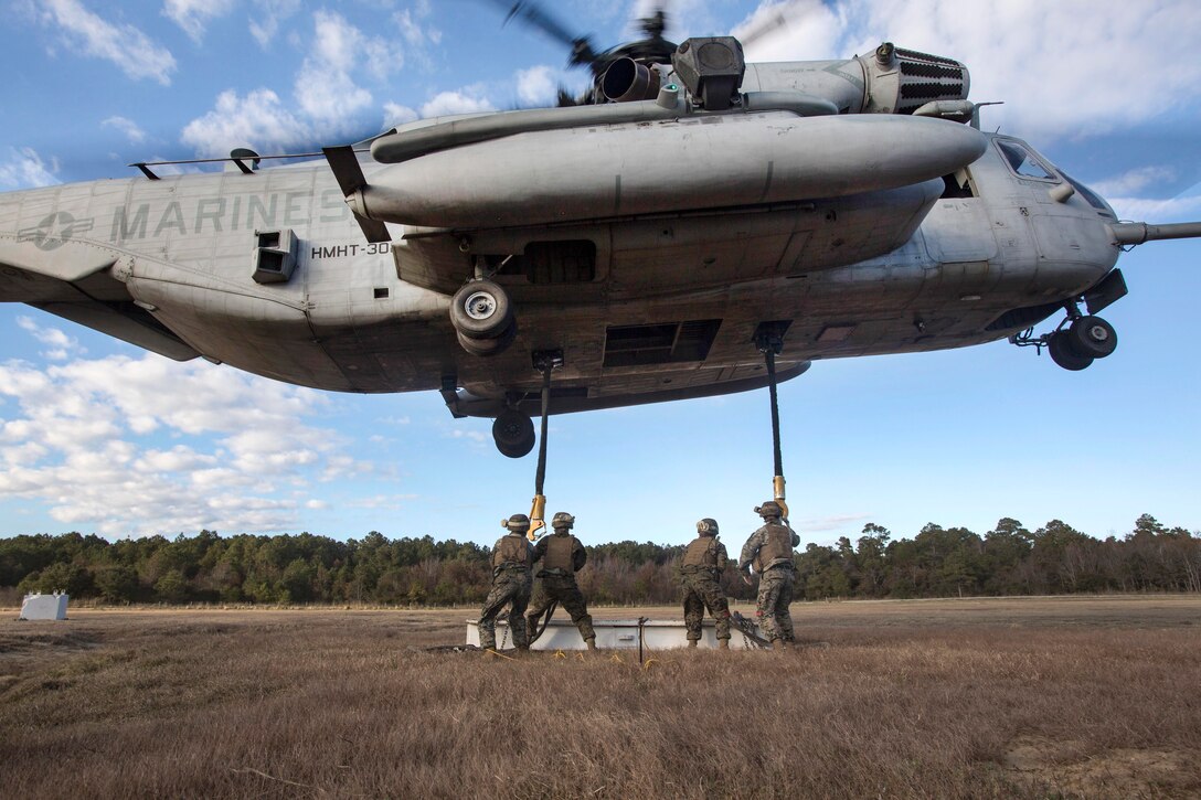 Marines attach cables and practice materials to a CH-53E Super Stallion helicopter during hoist training.