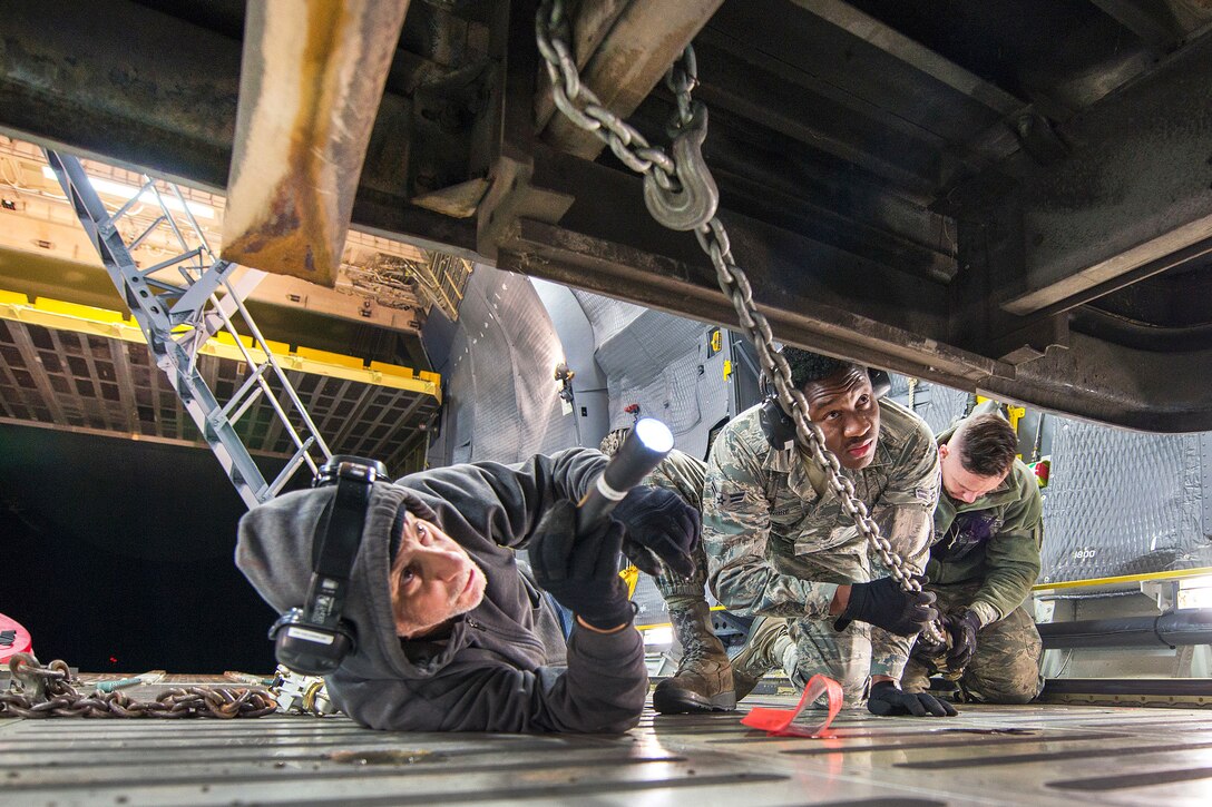 Airmen secure chains from buses to the aircraft floor on a C-5M Super Galaxy aircraft at Travis Air Force Base, Calif.