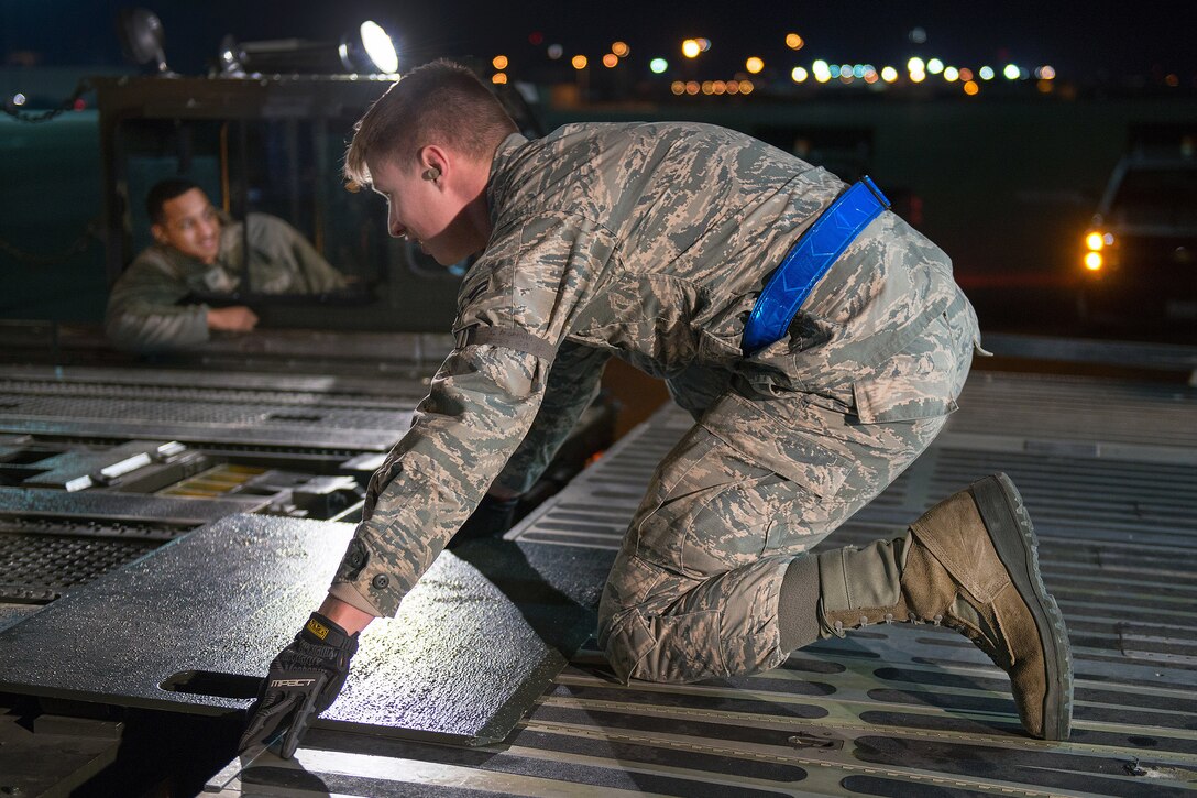 An airman places a panel on a C-5M Super Galaxy aircraft so they can load buses at Travis Air Force Base, Calif.