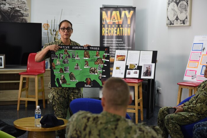 A service member teaches other service members holding a poster.