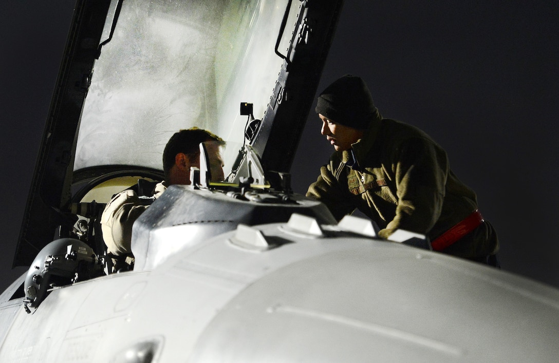 An Air Force crew chief assists a pilot with his gear inside the cockpit of an F-16 Fighting Falcon before a mission from Bagram Airfield, Afghanistan.