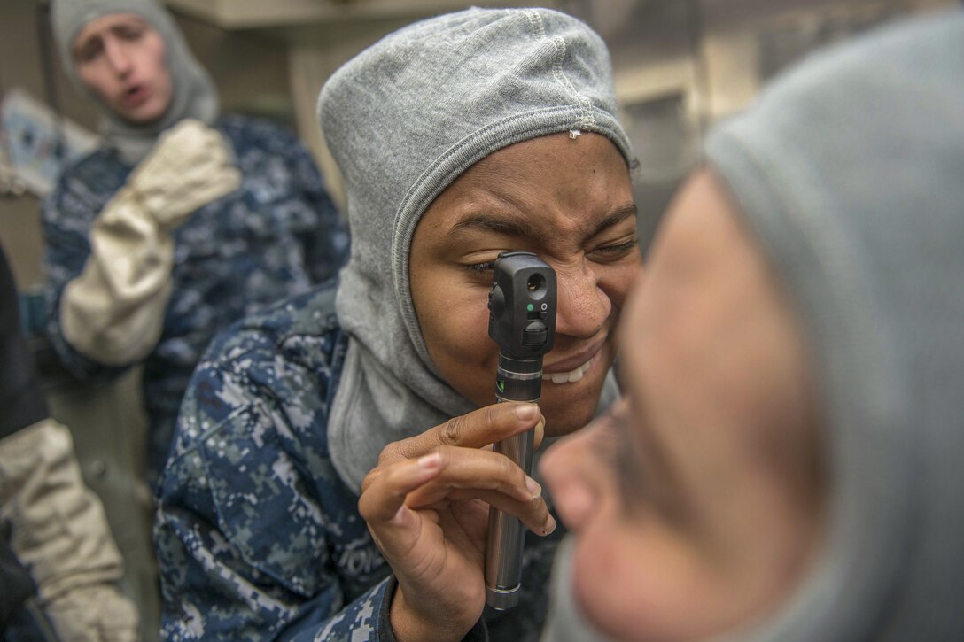 A sailor practices using an ophthalmoscope to examine eyes.