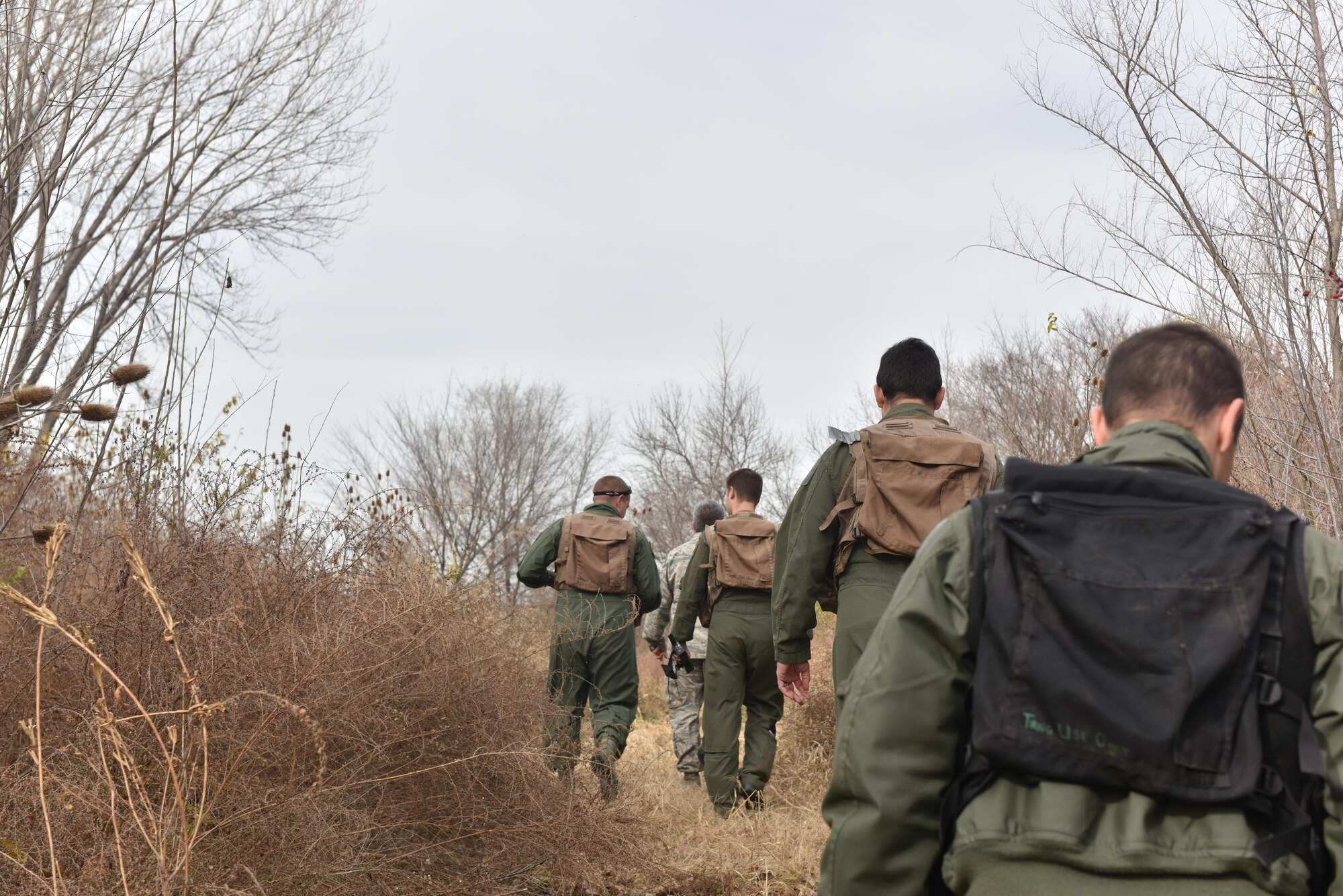 US Air Force Tech. Sgt. Sergio Avalos, a survival, evasion, resist and escape (SERE) specialist, trek through bushes with pilots of Team Whiteman to a designated starting area to conduct the navigation portion of their SERE training Nov.27, 2017 at Whiteman Air Force Base, Missouri. During this portion the pilots are must use given coordinates to locate a meeting point with the SERE instructor.