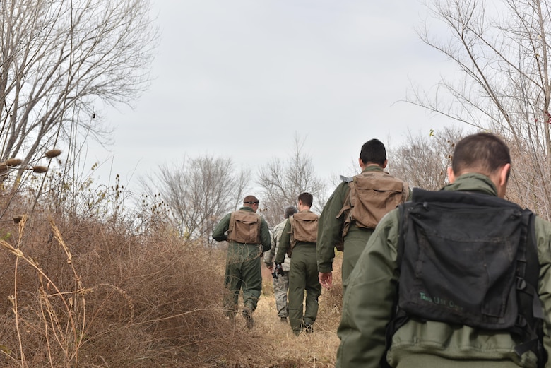 US Air Force Tech. Sgt. Sergio Avalos, a survival, evasion, resist and escape (SERE) specialist, trek through bushes with pilots of Team Whiteman to a designated starting area to conduct the navigation portion of their SERE training Nov.27, 2017 at Whiteman Air Force Base, Missouri. During this portion the pilots are must use given coordinates to locate a meeting point with the SERE instructor.