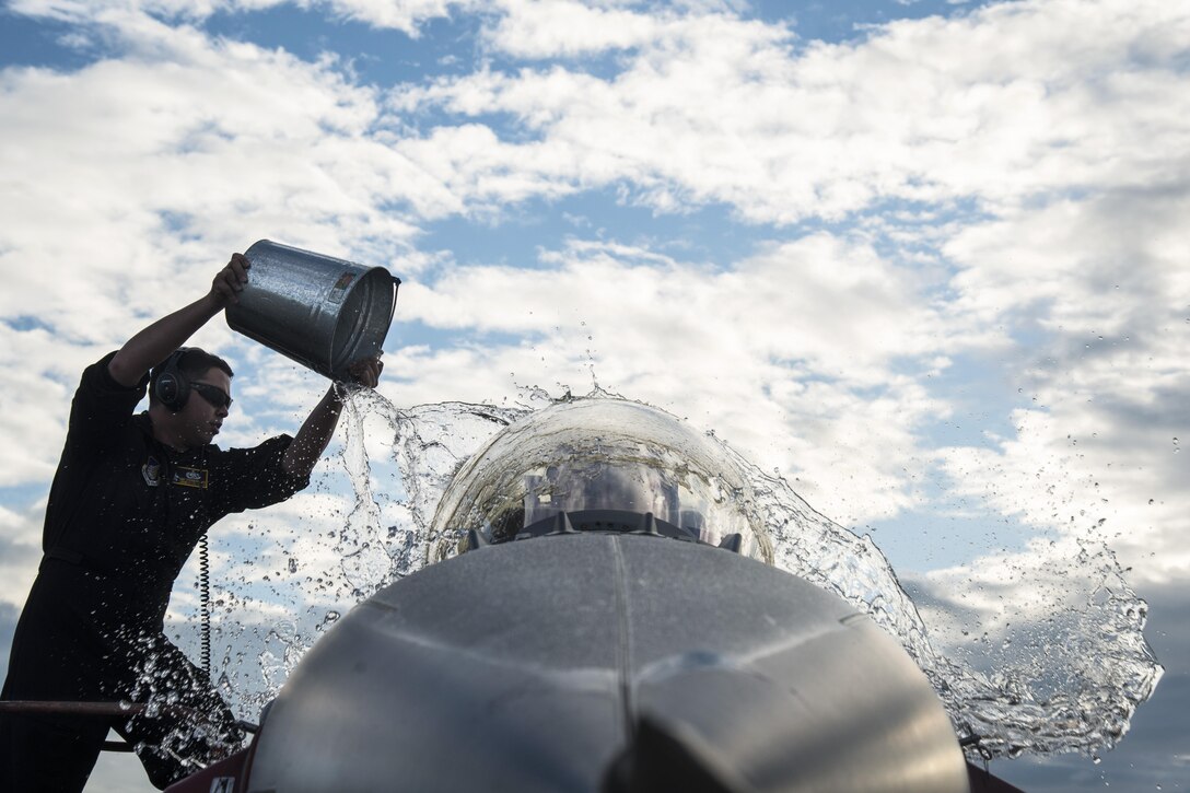 An airman throws water on an F-16 Fighting Falcon aircraft.