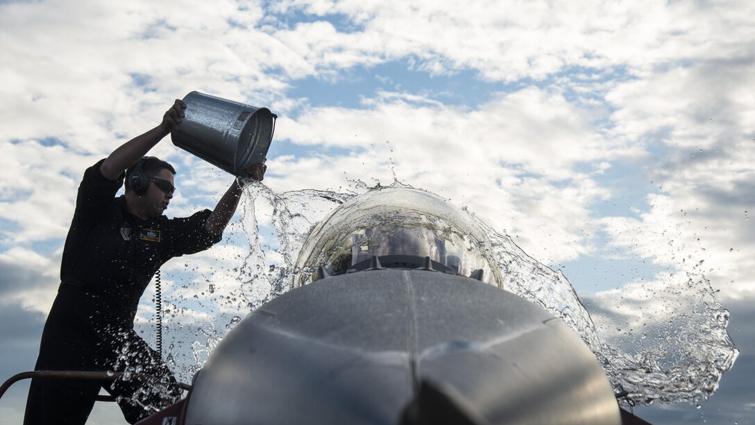 An airman throws water on an F-16 Fighting Falcon aircraft.