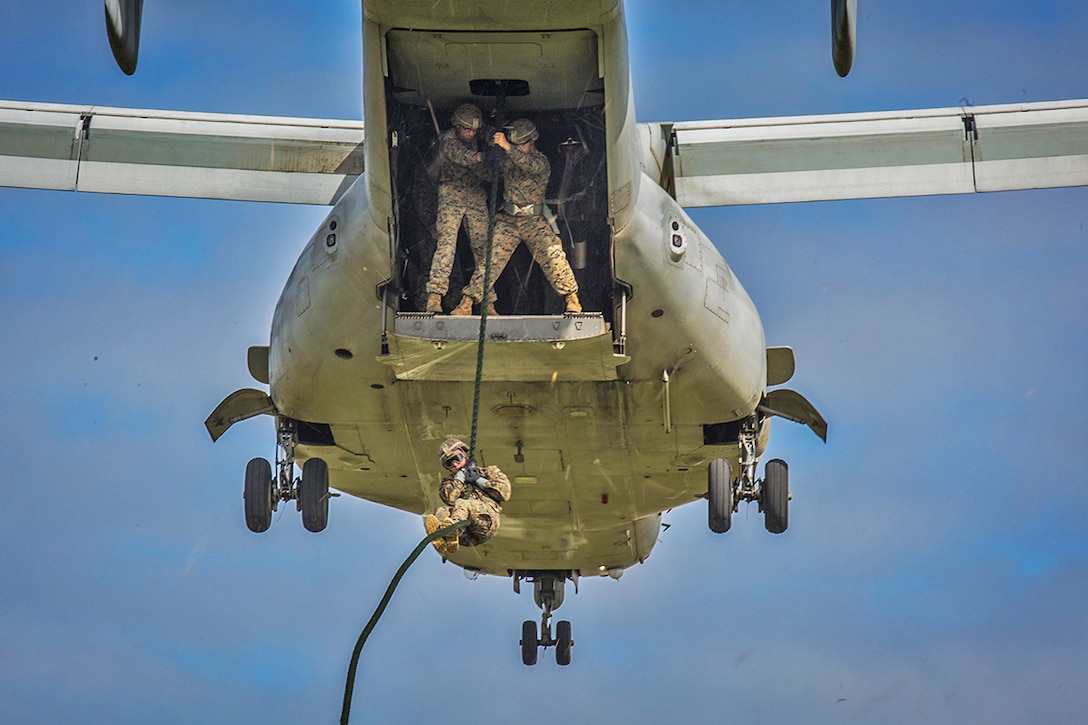 A Marine uses a rope to exit and descend from a hovering Osprey.